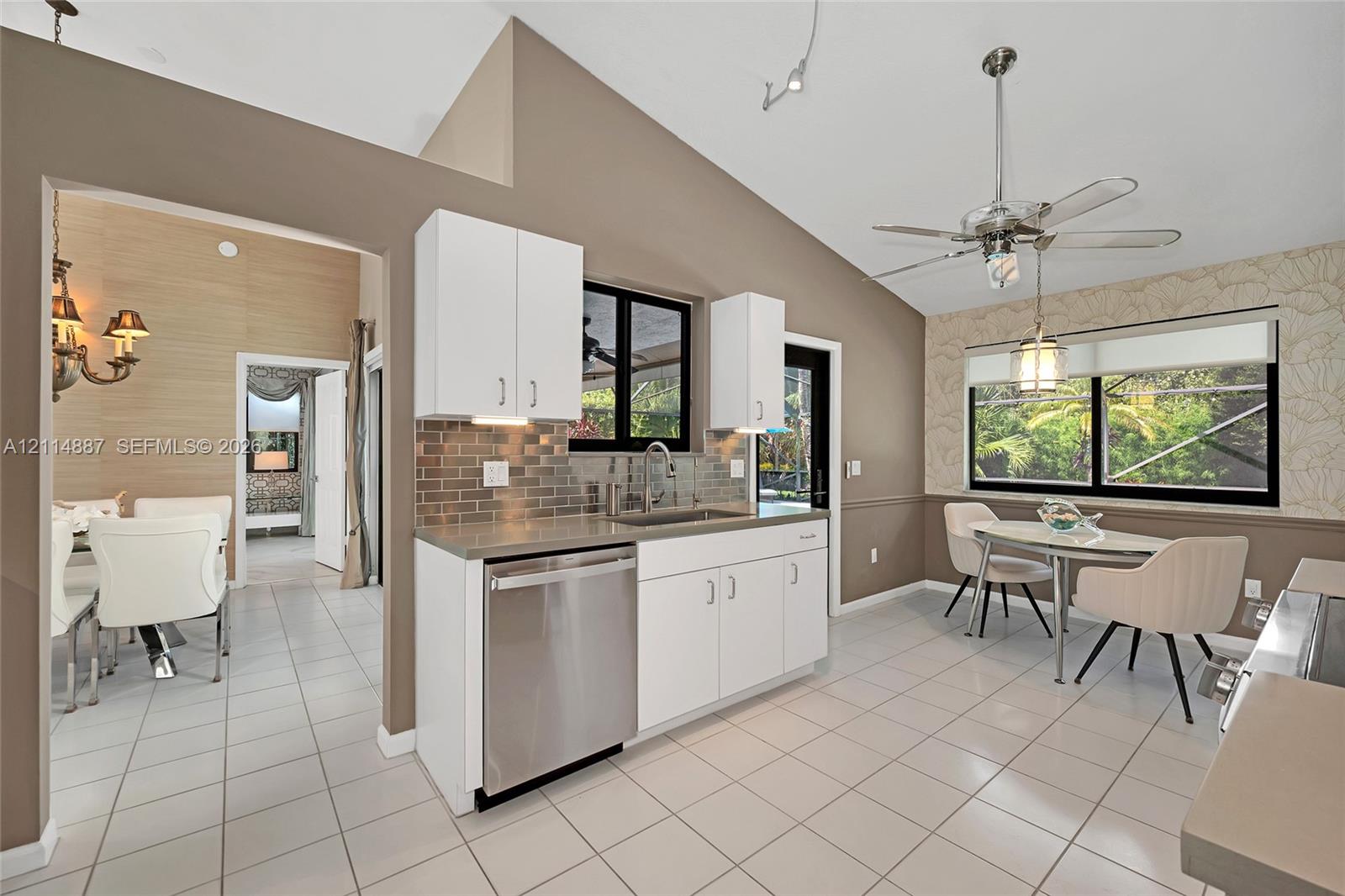 Kitchen featuring vaulted ceilings, white cabinetry, tile flooring, stainless steel dishwasher, and horizontal tile backsplash