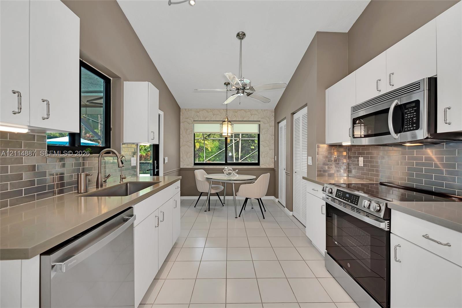 Kitchen featuring white shaker-style cabinetry, quartz countertops, stainless steel appliances, subway tile backsplash, and vaulted ceilings