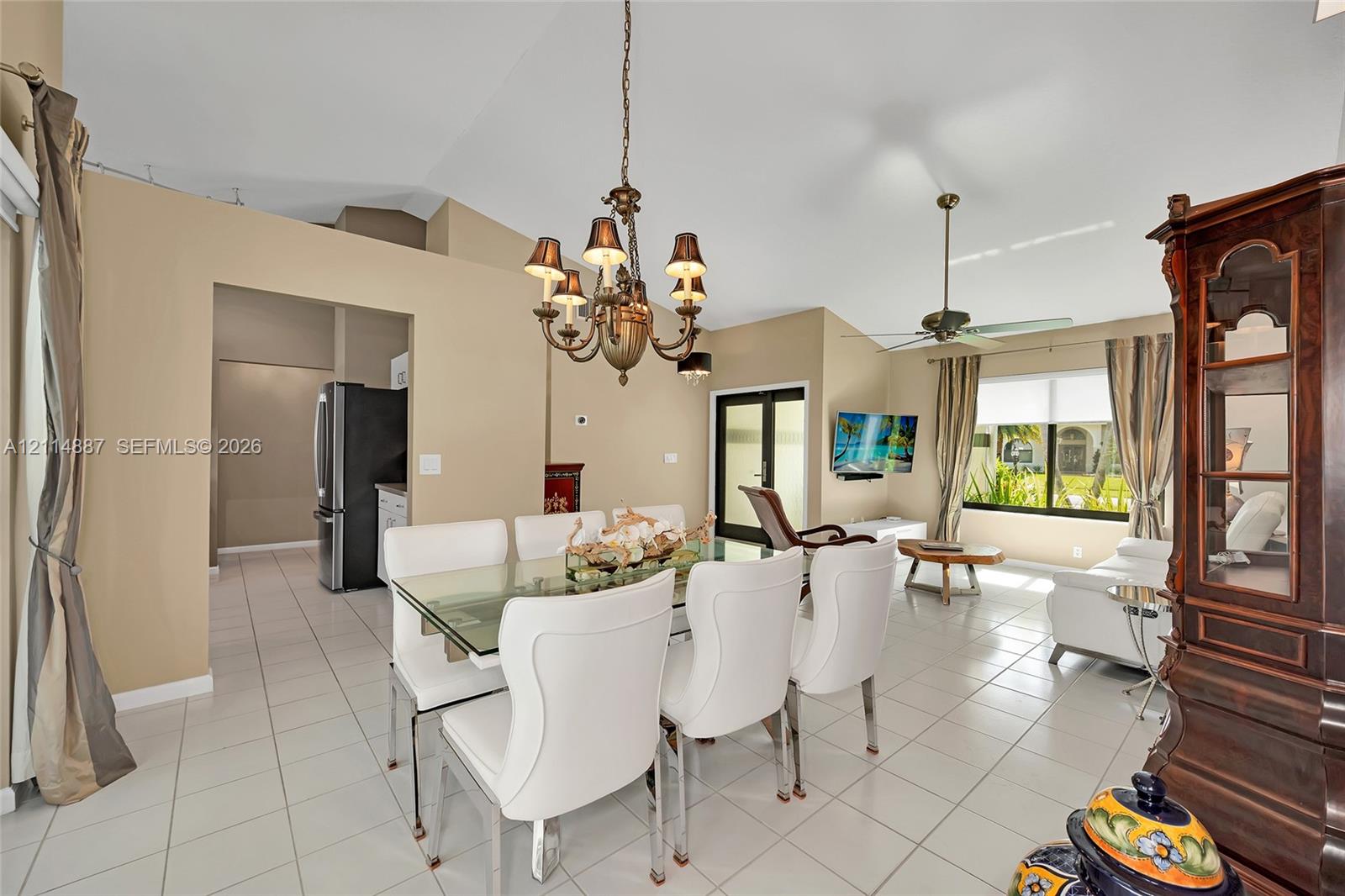 Open-concept area featuring vaulted ceilings, neutral wall tones, ceramic tile flooring, a multi-arm chandelier, and a ceiling fan