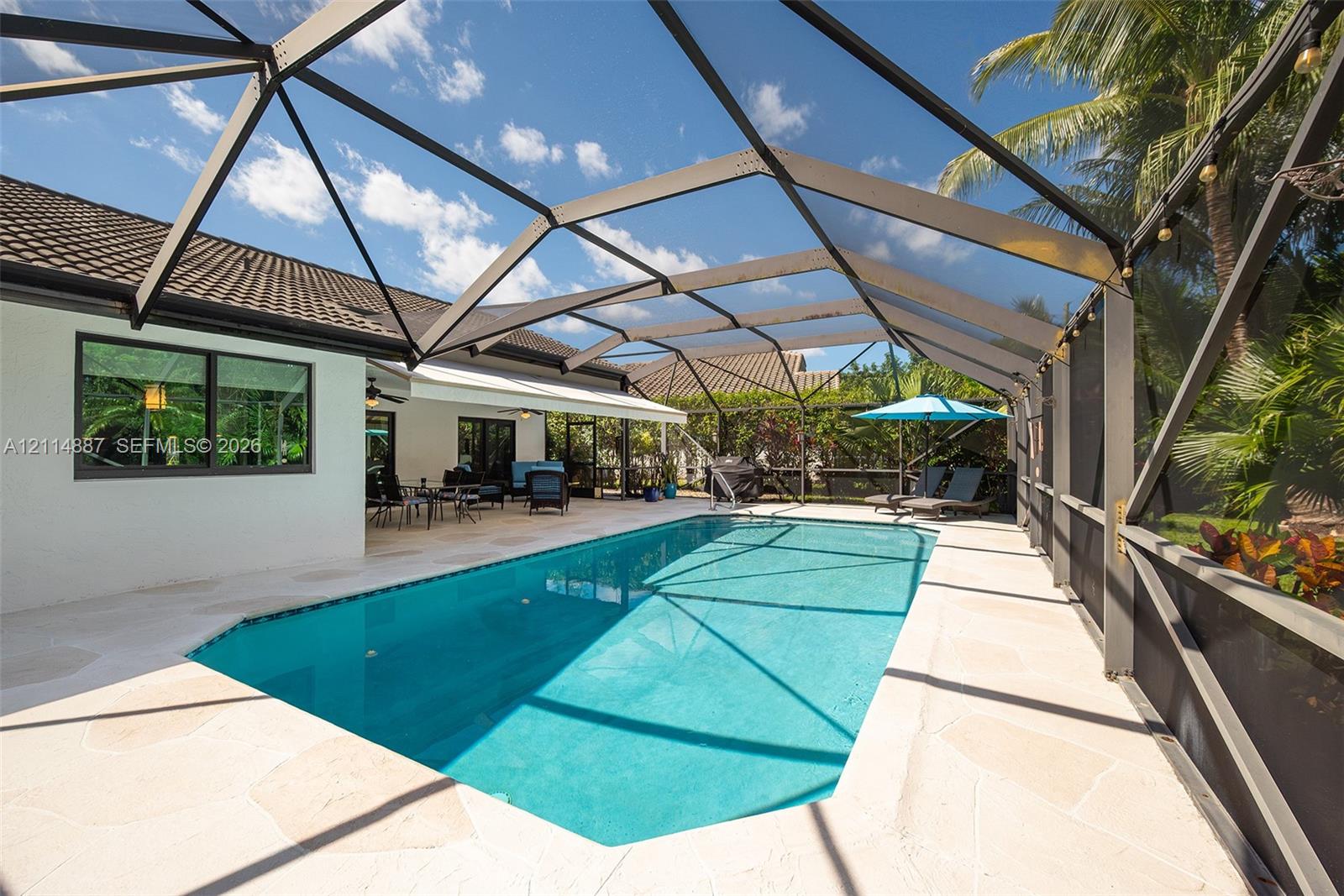 Screen-enclosed swimming pool featuring a light-toned stone deck, integrated gutter system, and covered patio area