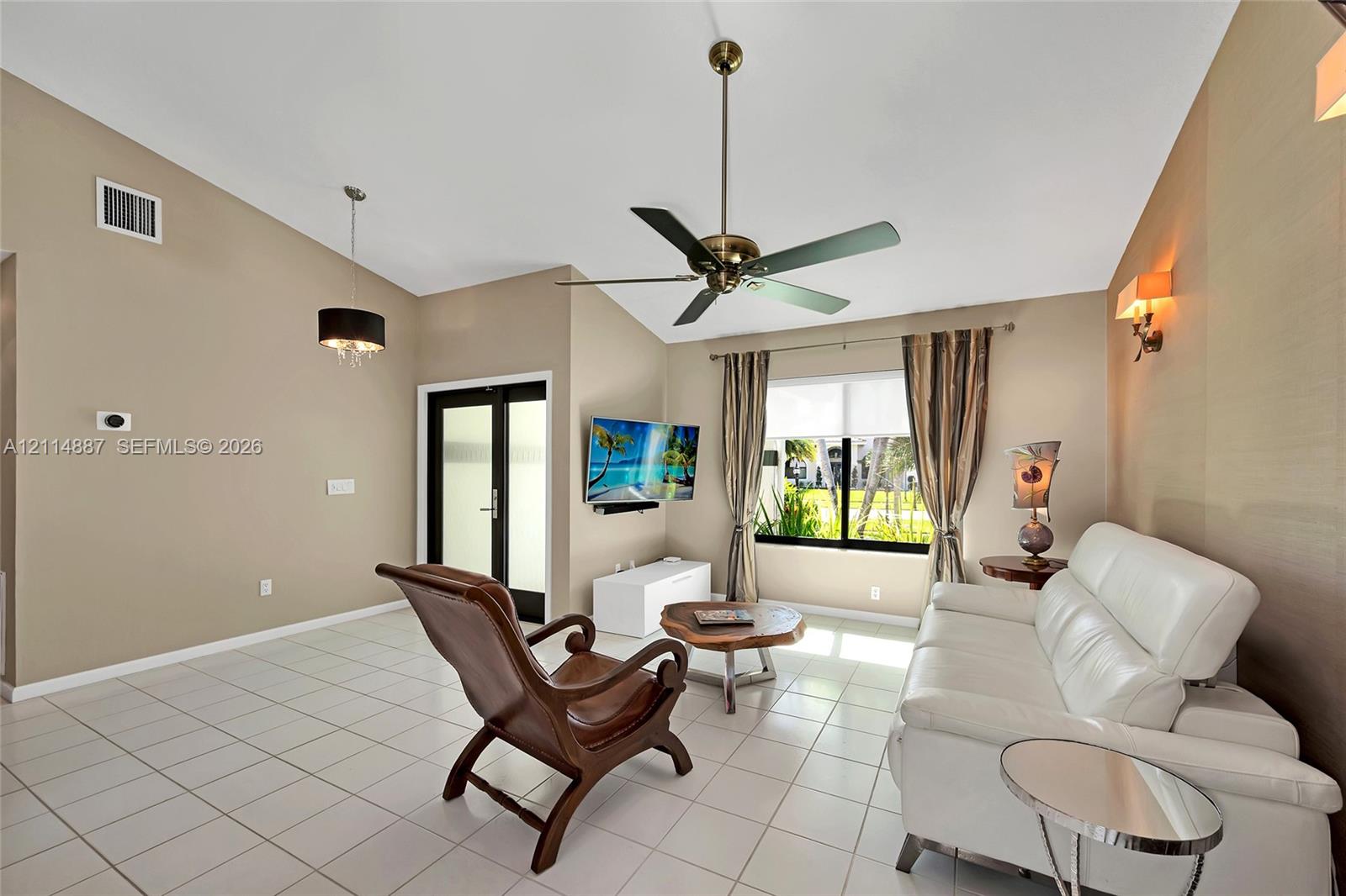 Vaulted ceiling with an integrated multi-blade ceiling fan, neutral wall finishes, tile flooring, and custom wall-mounted lighting fixtures