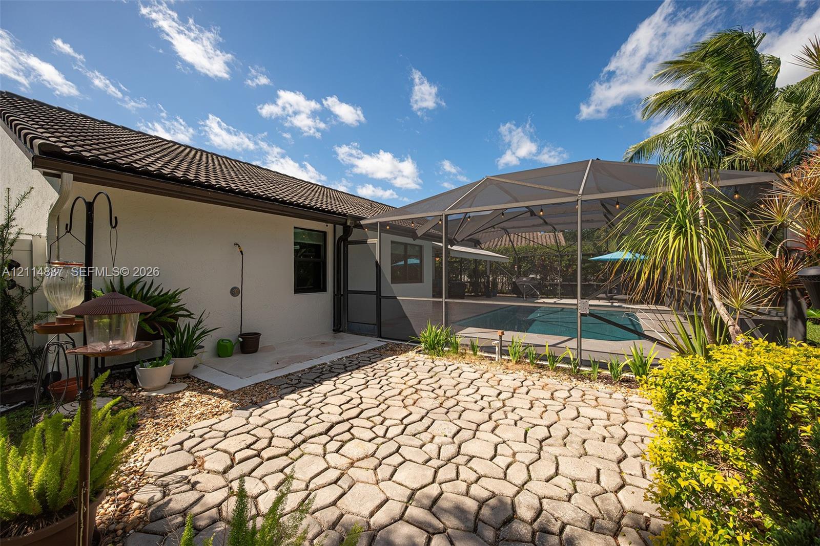 Backyard featuring a stone-patterned paver patio, screened-in swimming pool enclosure, stucco exterior, and tile roofing