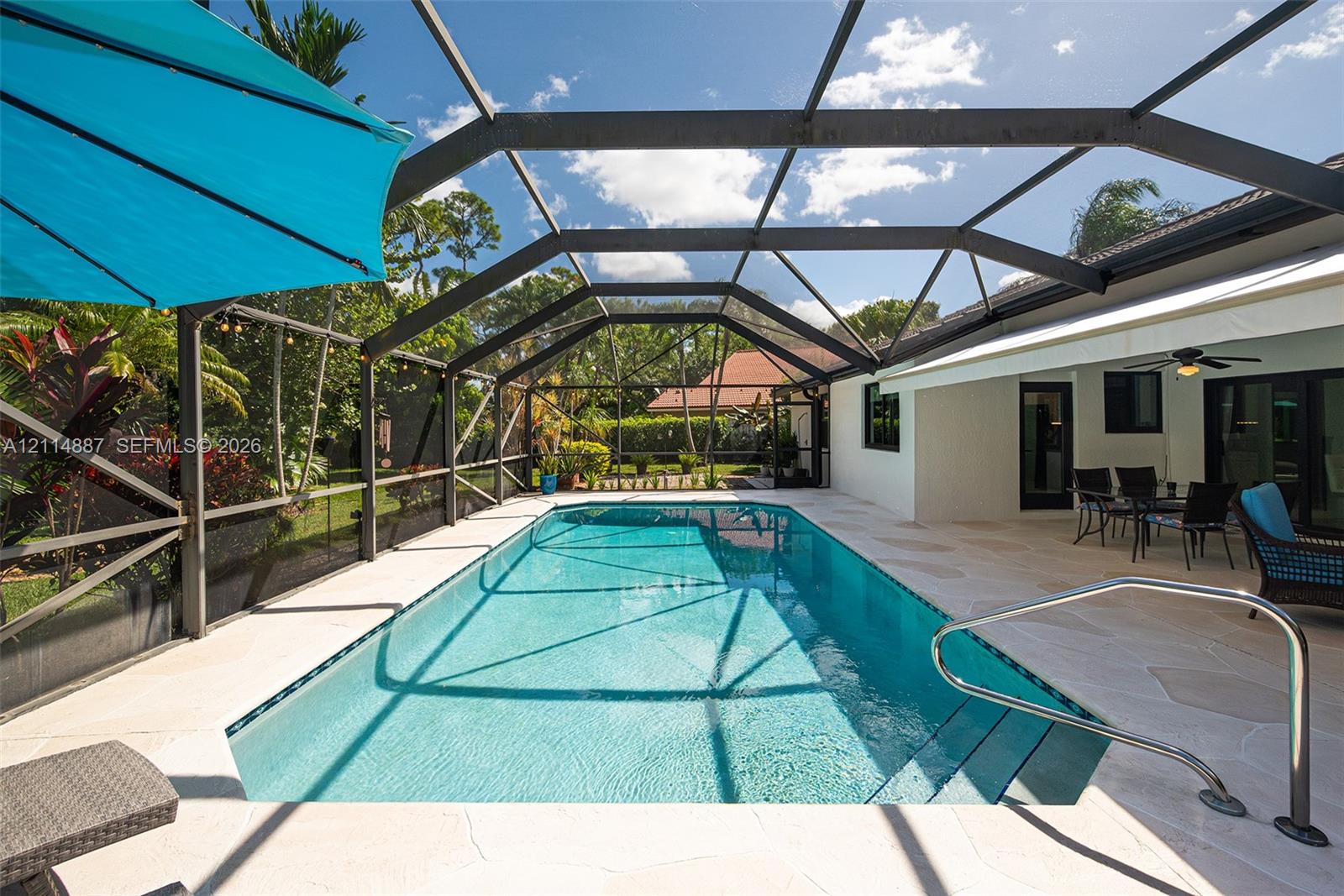 Screen-enclosed rectangular swimming pool with built-in stairs, metal handrail, and light-toned paver pool deck