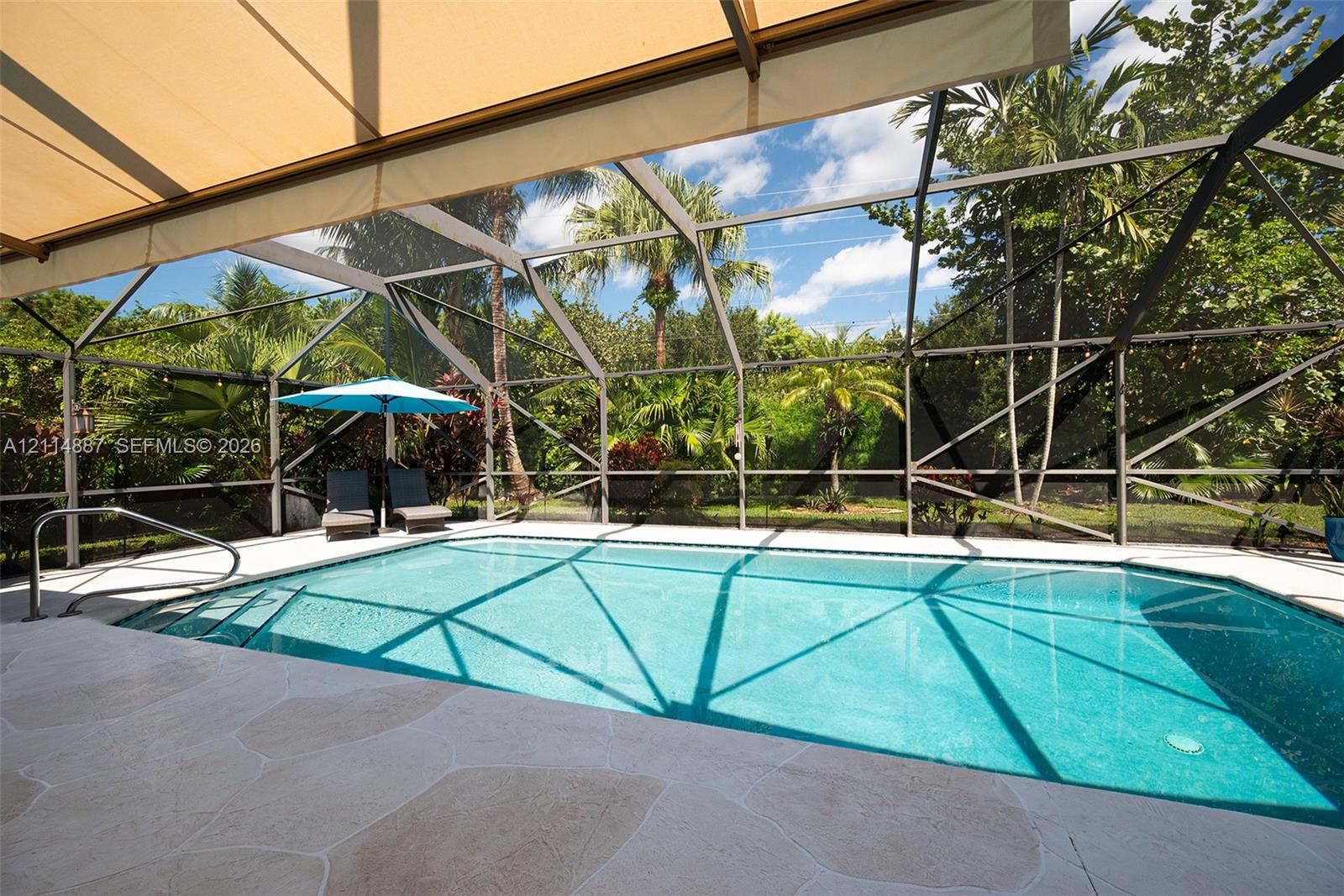 Screened-in pool area featuring a stone-paver deck, built-in metal handrails, and a retractable fabric awning