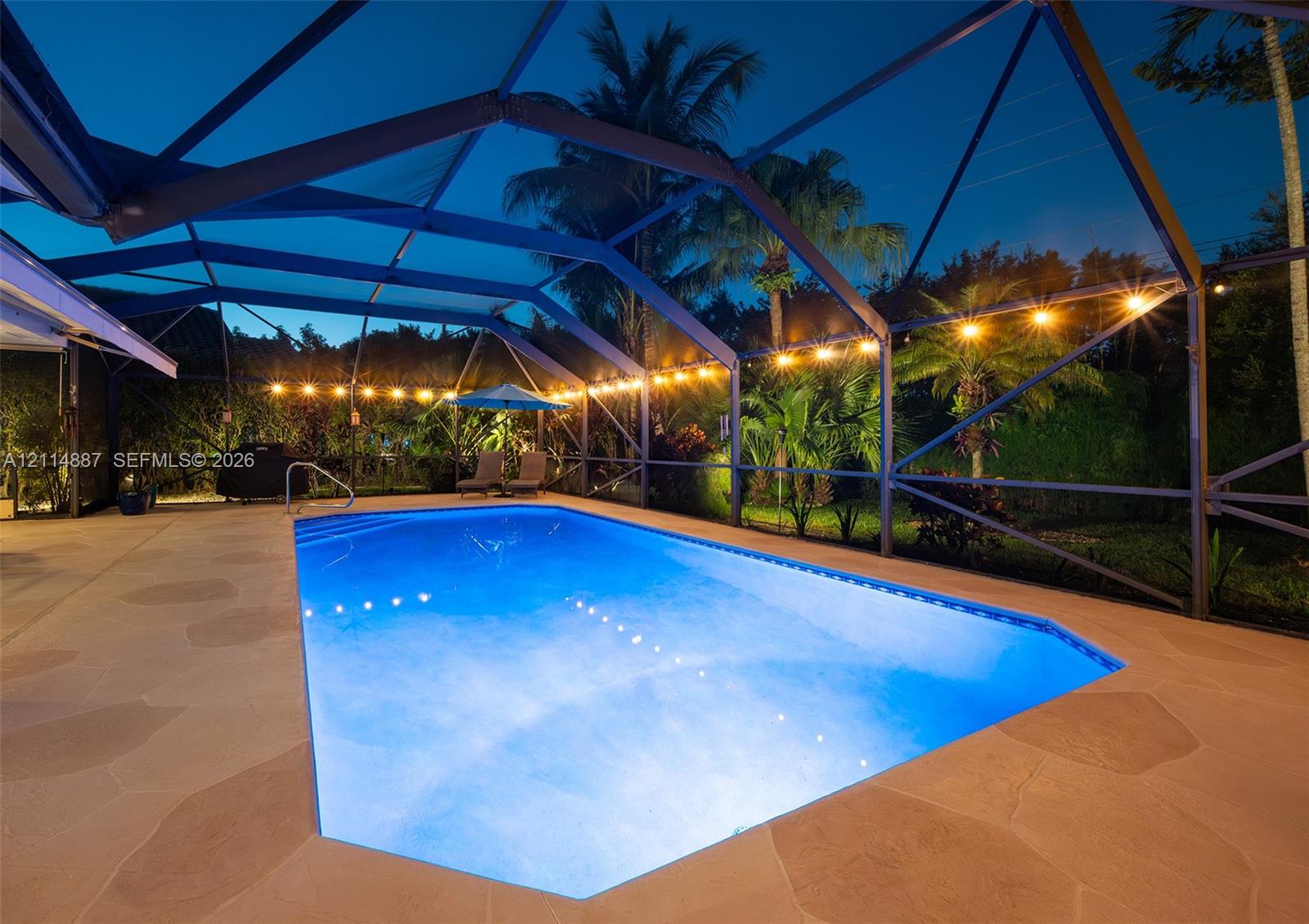 Screen-enclosed swimming pool featuring a natural stone-style deck, integrated pool lighting, and built-in metal handrail