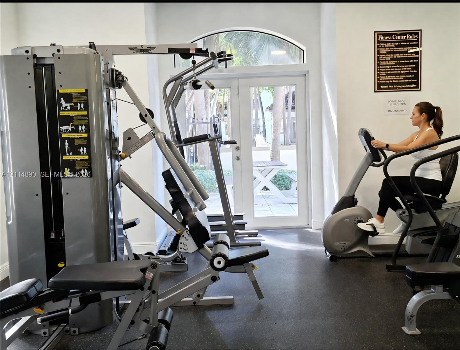 Fitness center featuring industrial-grade weight training equipment, cardio machines, resilient rubber flooring, and arched double-glass entry doors