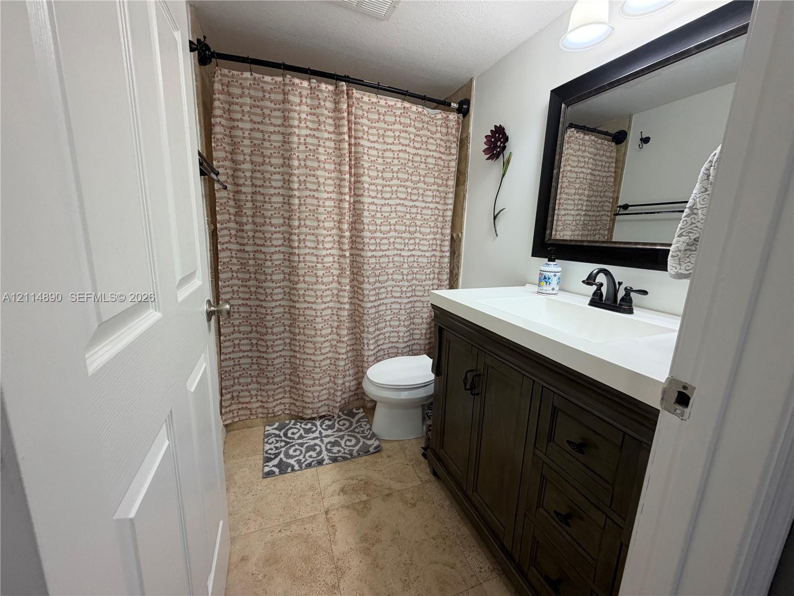 Bathroom featuring a vanity with dark wood-finish cabinetry, a white countertop with an integrated sink, a dark-framed mirror, and a curved shower rod