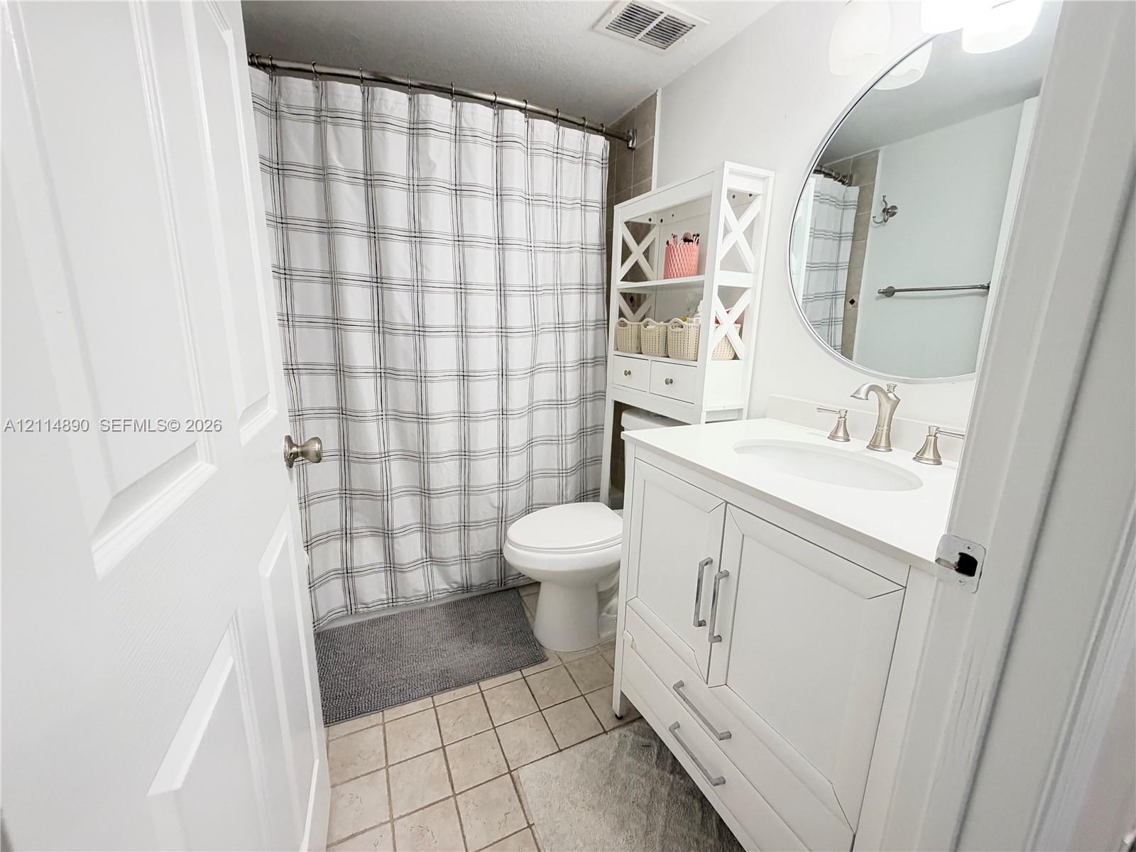 White vanity cabinet with a stone-composite countertop, undermount sink, brushed nickel faucet, and circular wall mirror with integrated lighting