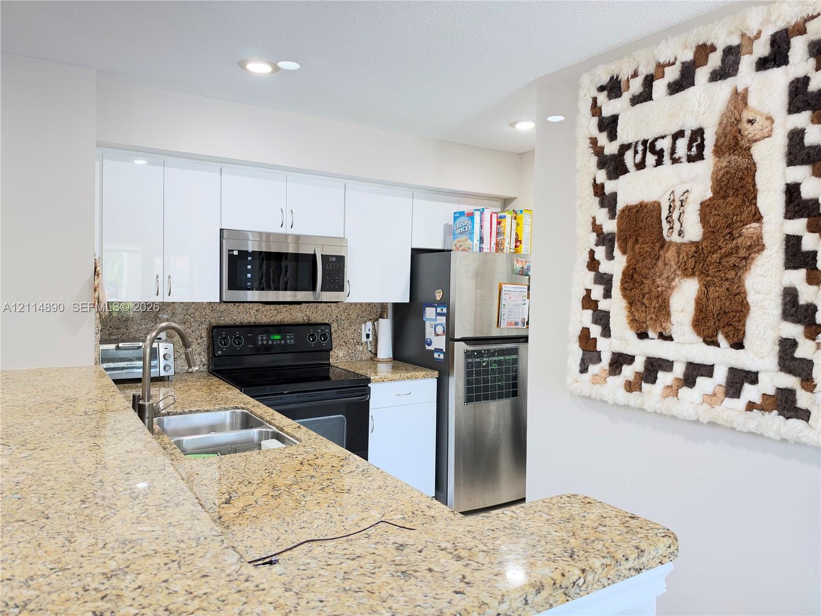 Kitchen featuring white cabinetry, stone countertops, stainless steel appliances, and a dual-basin sink with a goose-neck faucet