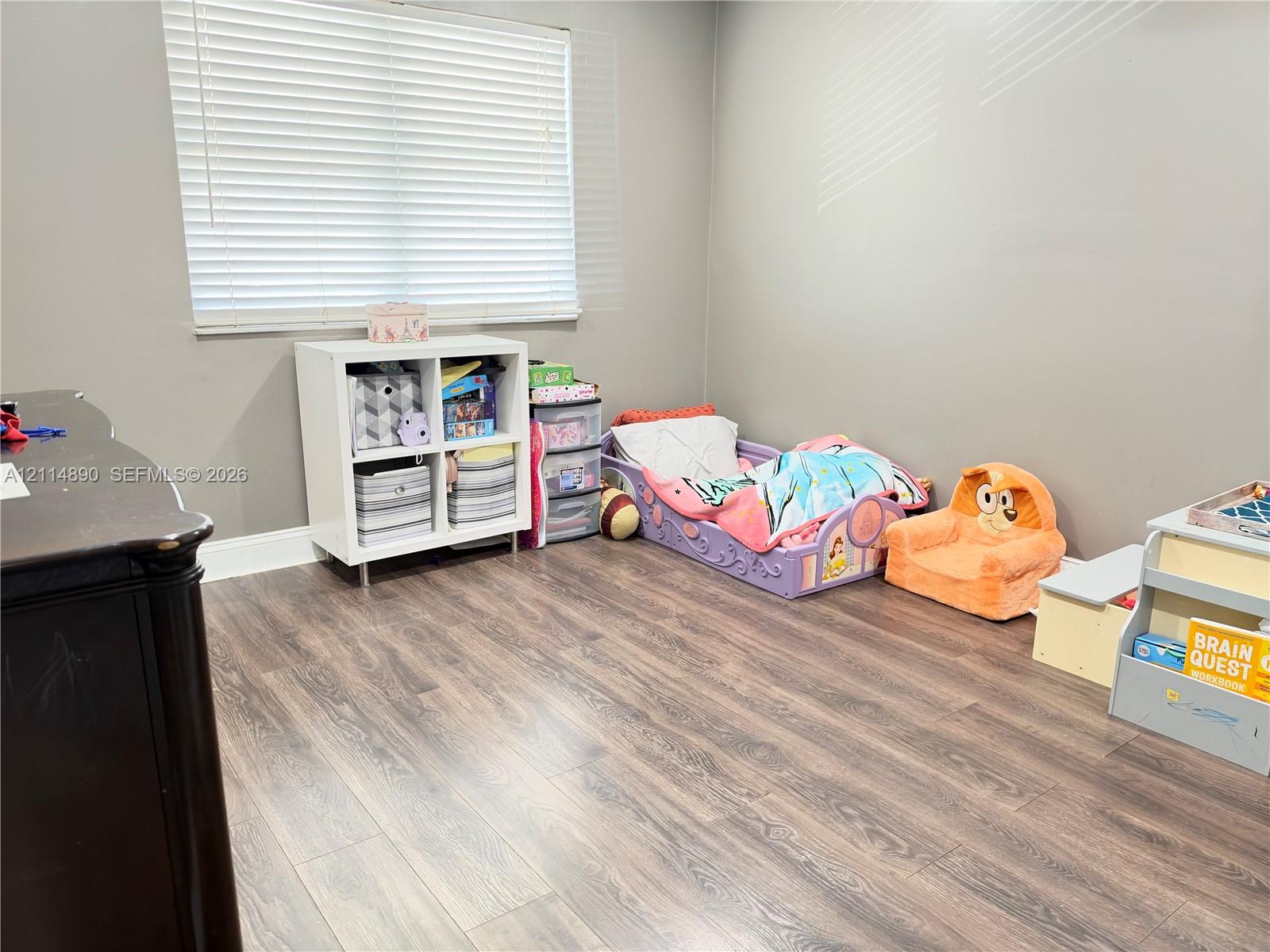 Neutral-toned interior space featuring wood-finish flooring and a horizontal window with adjustable blinds