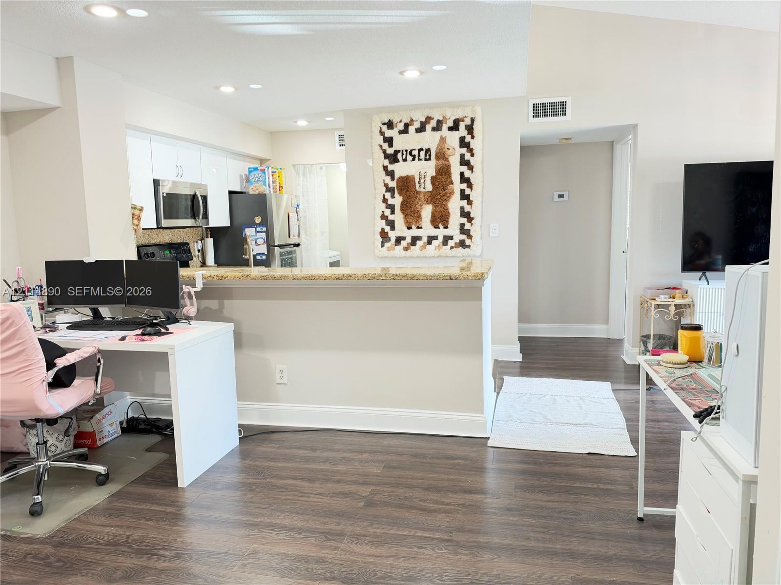 Kitchen featuring white cabinetry, stone-finish countertops, stainless steel microwave, and recessed ceiling lighting over wood-finish flooring