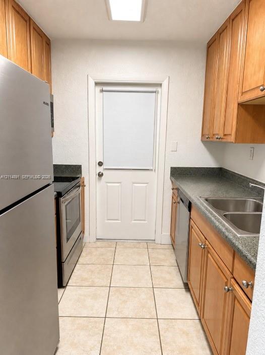 Kitchen featuring wood cabinetry, stone-finish countertops, stainless steel appliances, double-basin sink, and tile flooring Kitchen featuring wood cabinetry, stone-finish countertops, stainless steel appliances, double-basin sink, and tile flooring