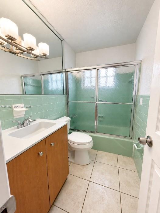 Bathroom featuring a wood-finish vanity with a rectangular sink, full-width mirror, tile surround tub-shower with sliding glass doors, and tile flooring Bathroom featuring a wood-finish vanity with a rectangular sink, full-width mirror, tile surround tub-shower with sliding glass doors, and tile flooring