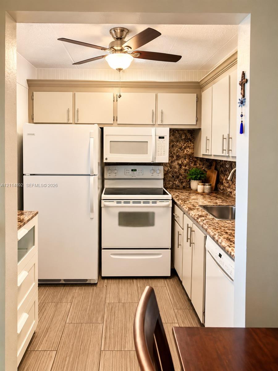 Kitchen featuring white cabinetry with metallic pulls, patterned laminate countertops, a stainless steel sink, wood-finish tile flooring, and a ceiling-mounted fan with integrated lighting