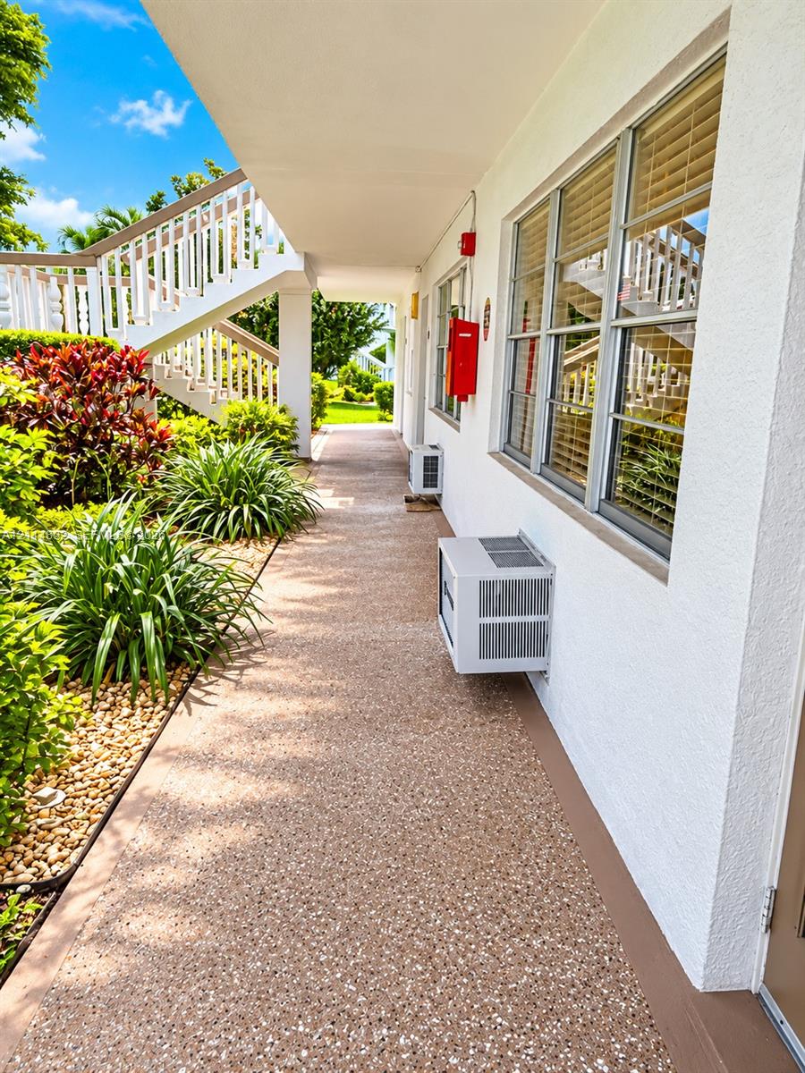 Exterior walkway featuring a pebble-finish surface, white stucco facade, multi-pane windows with integrated blinds, and built-in metal staircase railings