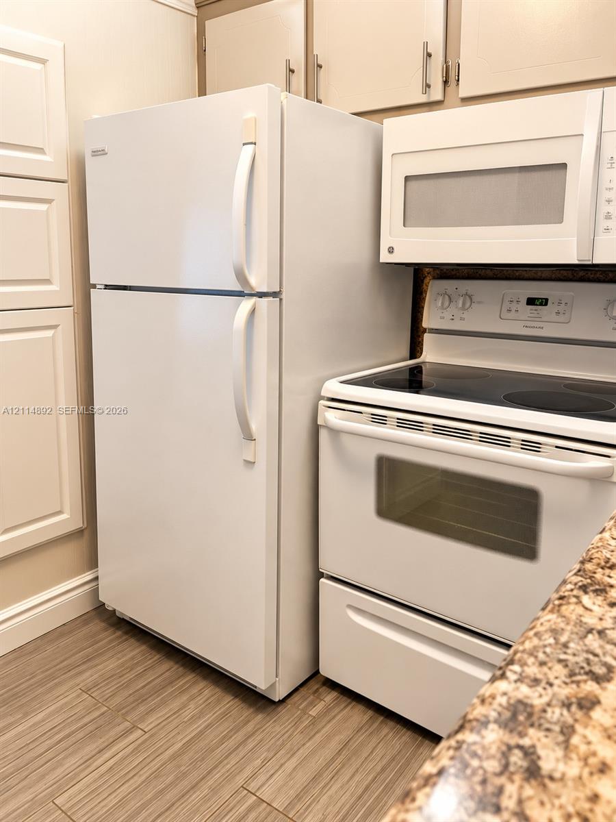 Kitchen featuring white upper cabinetry, a top-freezer refrigerator, over-the-range microwave, electric smooth-top range, and stone-finish countertops