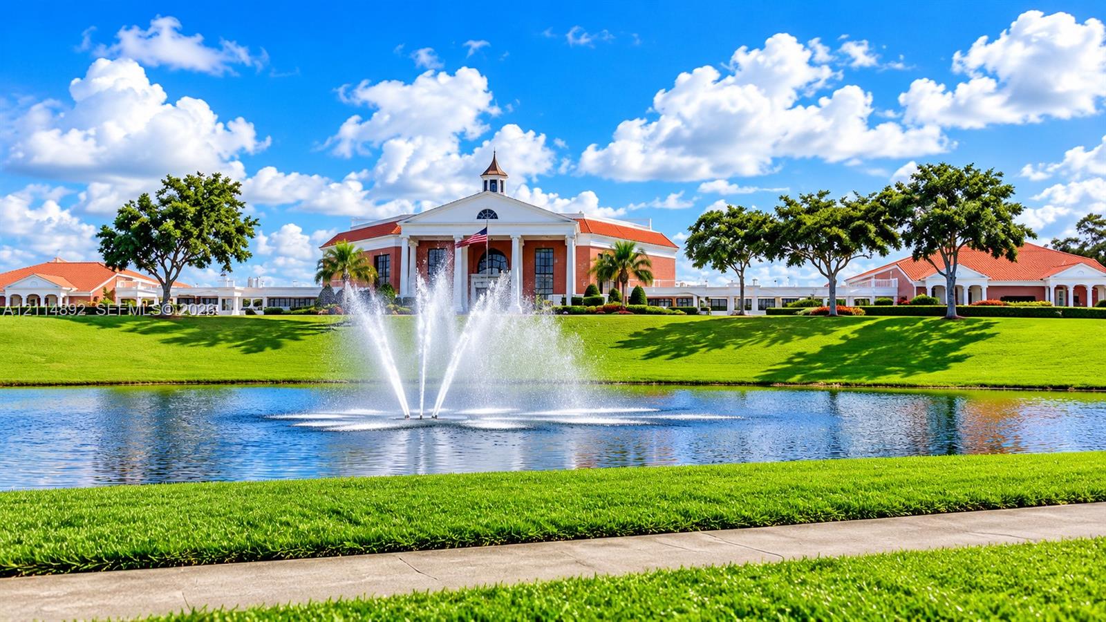 Colonial-style architecture featuring a central cupola and multi-columned portico, accented by a centered water fountain, surrounding pond, and expansive lawn