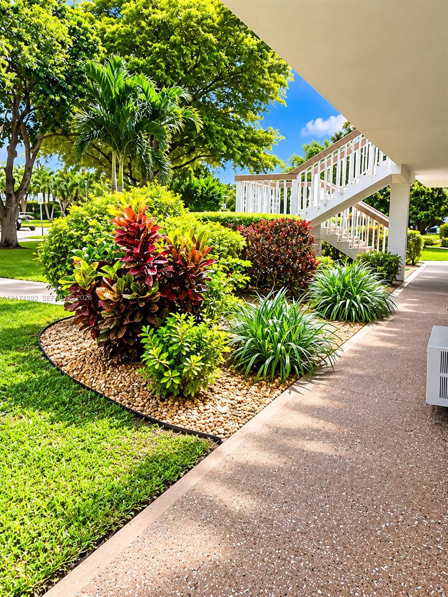 Landscaped garden featuring mature trees, colorful foliage, and decorative stone ground cover with concrete walkway and external staircase