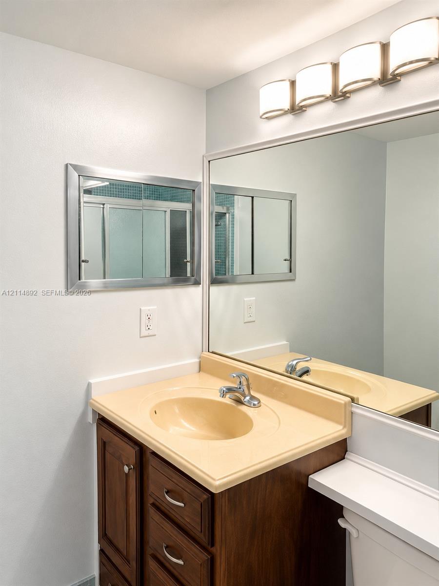 Vanity featuring a wood-finish cabinet, molded countertop with integrated basin, polished metal faucet, wall-to-wall mirror, and four-light vanity fixture
