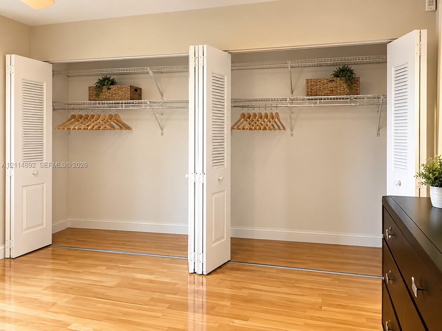 Reach-in closet featuring white louvered bi-fold doors, wire shelving, and wood-finish flooring