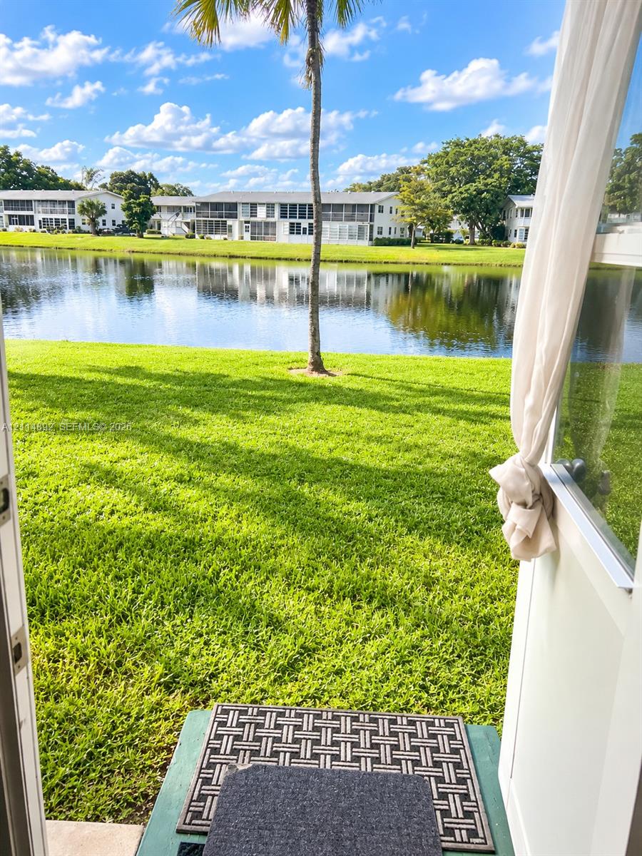 Waterfront property featuring a manicured lawn, pond frontage, and mature palm tree