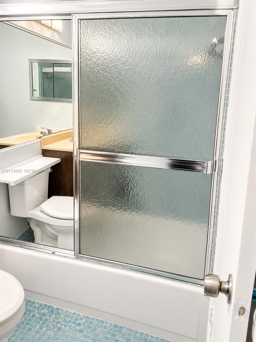 Shower enclosure featuring textured glass sliding doors with chrome framing, blue mosaic tile flooring, and a vanity with a recessed sink
