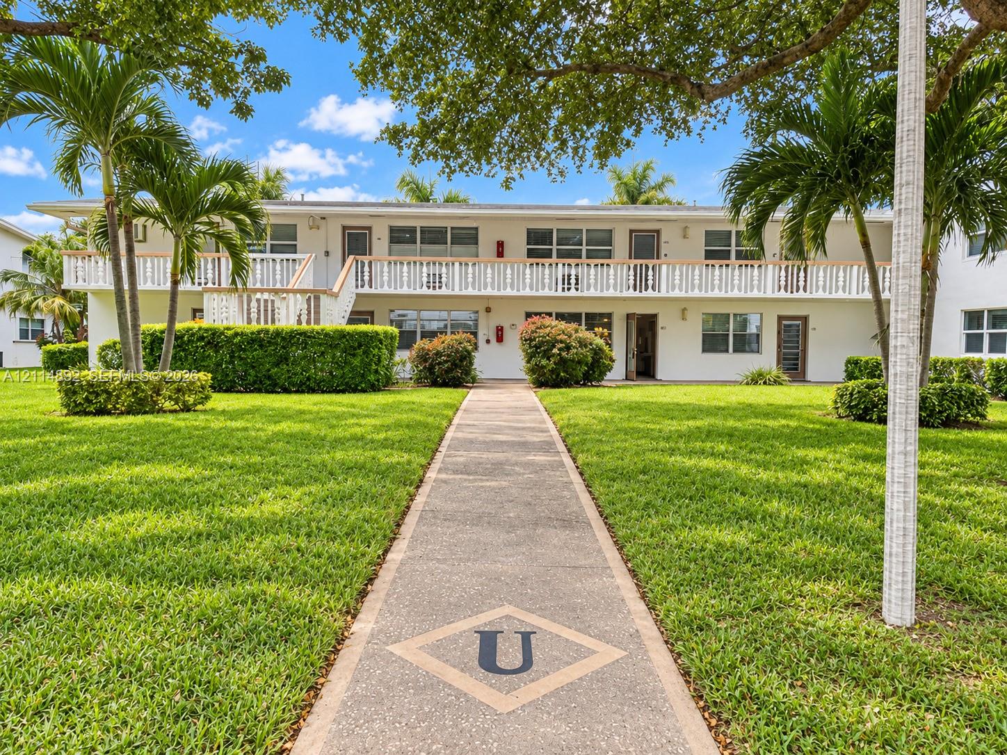 Two-story exterior featuring a decorative second-level balcony, paved walkway, manicured lawn, and mature landscaping