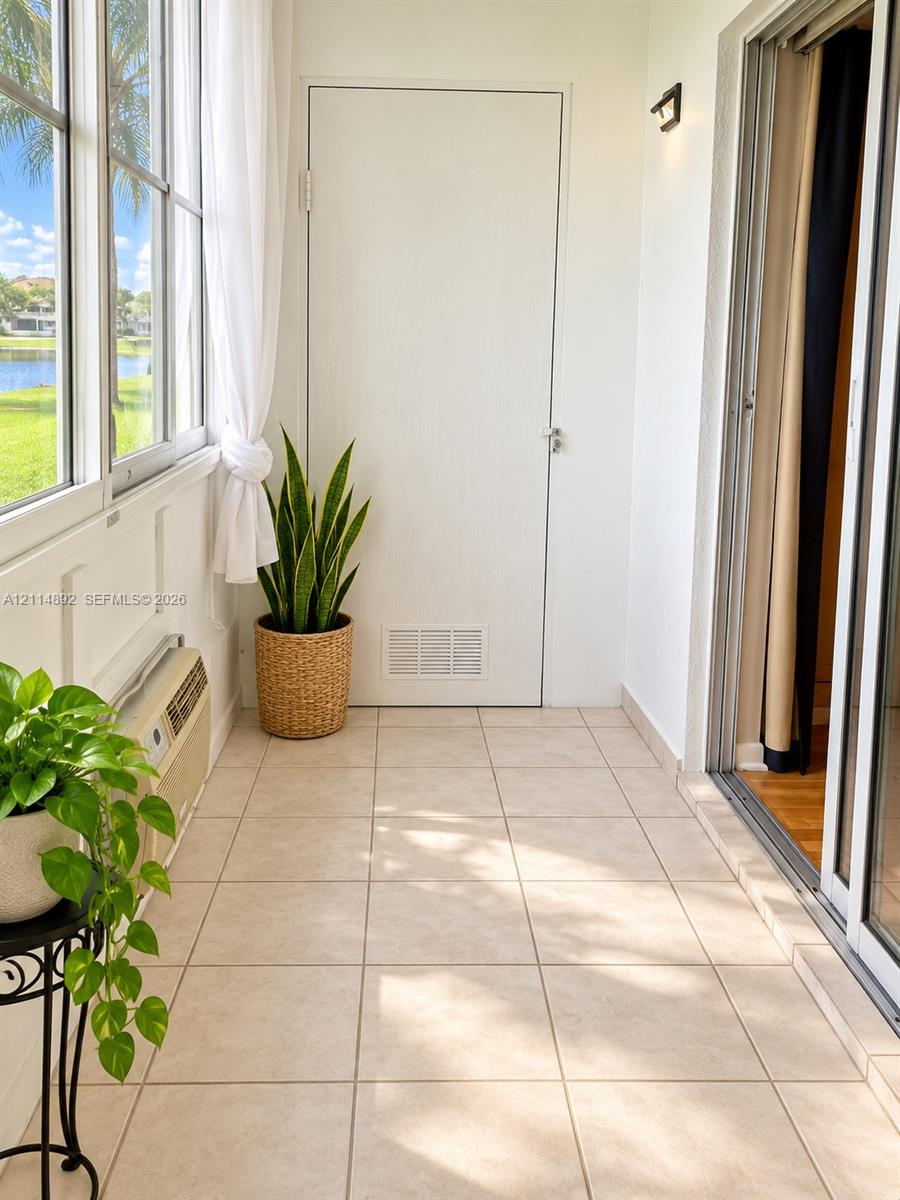 Enclosed patio featuring large-format tile flooring, expansive windows, wall-mounted lighting, and a neutral white color palette