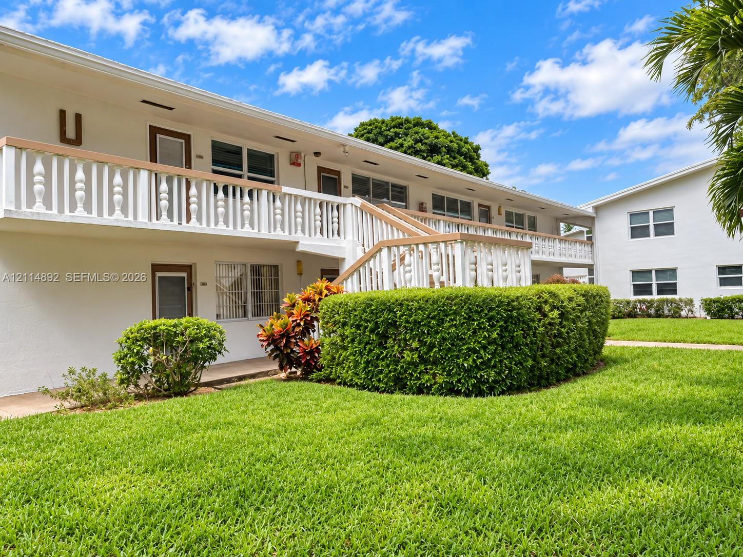 Two-story exterior featuring white stucco siding, a second-level balcony with decorative balustrades, an open-air staircase, and manicured landscaping
