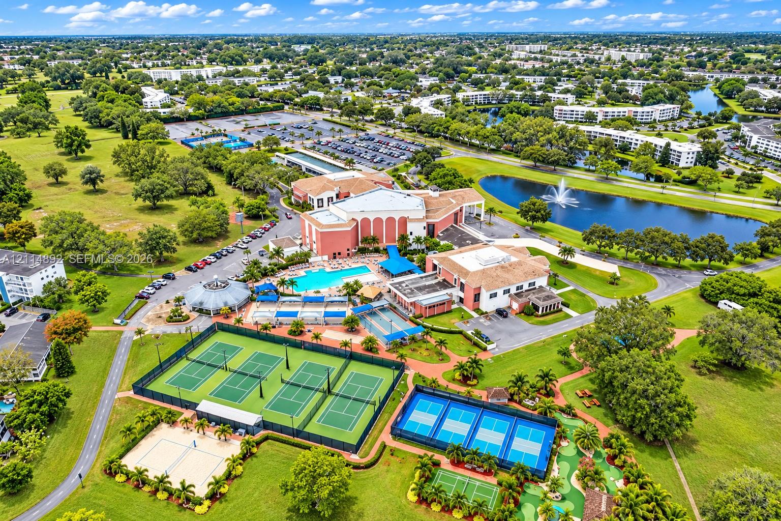 Aerial perspective of a multi-facility recreational complex featuring a swimming pool, multiple tennis courts, pickleball courts, and a putting green