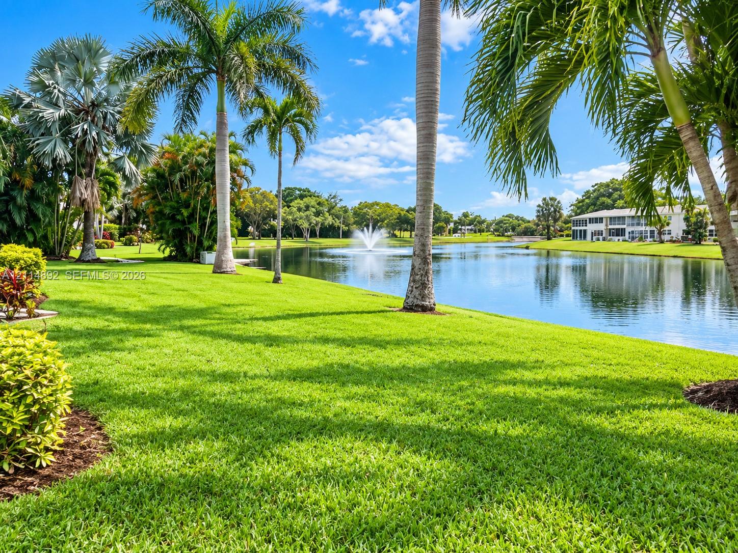 Expansive grounds featuring a manicured lawn, mature palm trees, a large pond, and a built-in water fountain