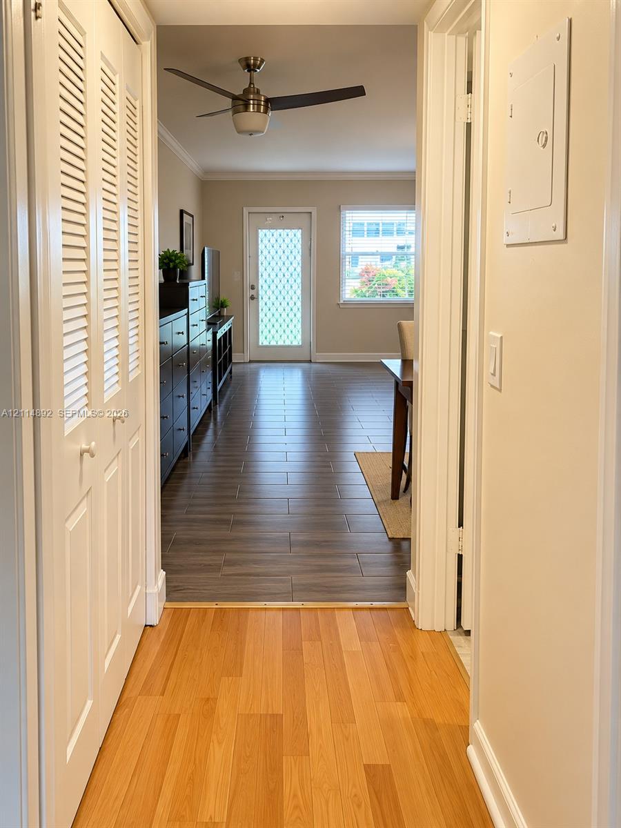 Interior hallway featuring light-toned wood-finish flooring, white louvered closet doors, and a ceiling-mounted fan in the common area with dark wood-finish tile flooring