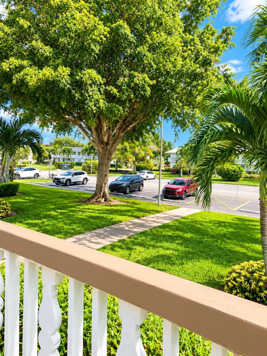 Outdoor space featuring a painted wood railing, paved pedestrian walkway, mature landscaping, and green lawn