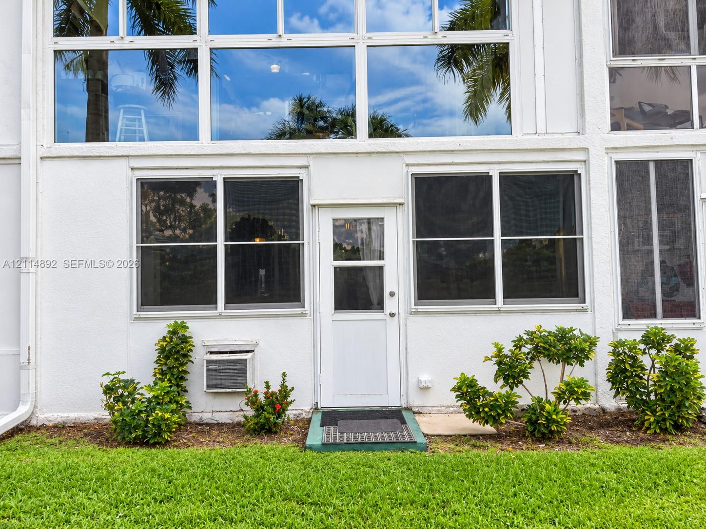 Exterior facade featuring multi-story window arrays, a central glass-panel entry door, and manicured foundation landscaping