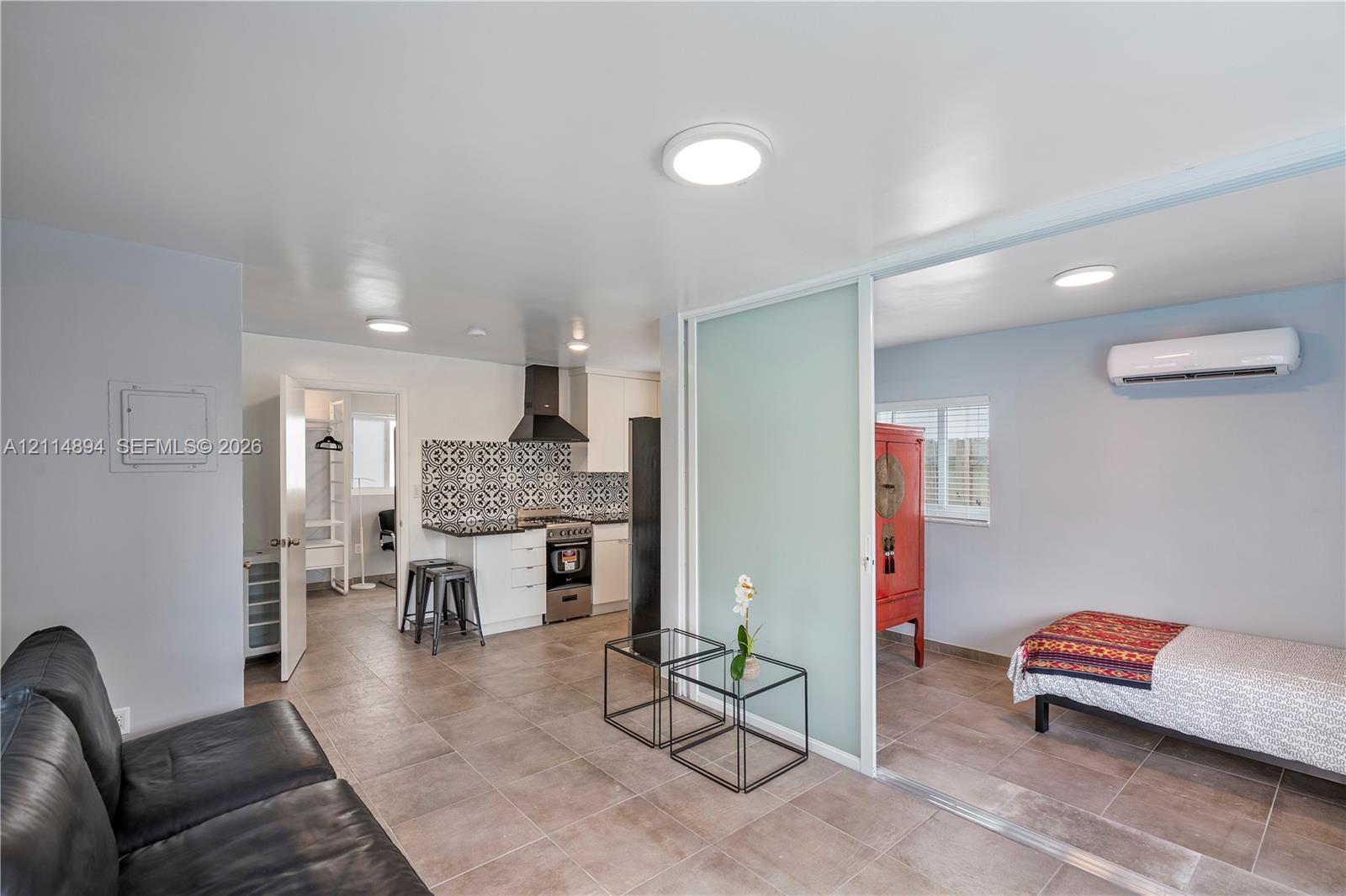 Large-format tile flooring, kitchen featuring patterned backsplash and stainless steel range, wall-mounted mini-split HVAC unit, and frosted glass sliding room divider