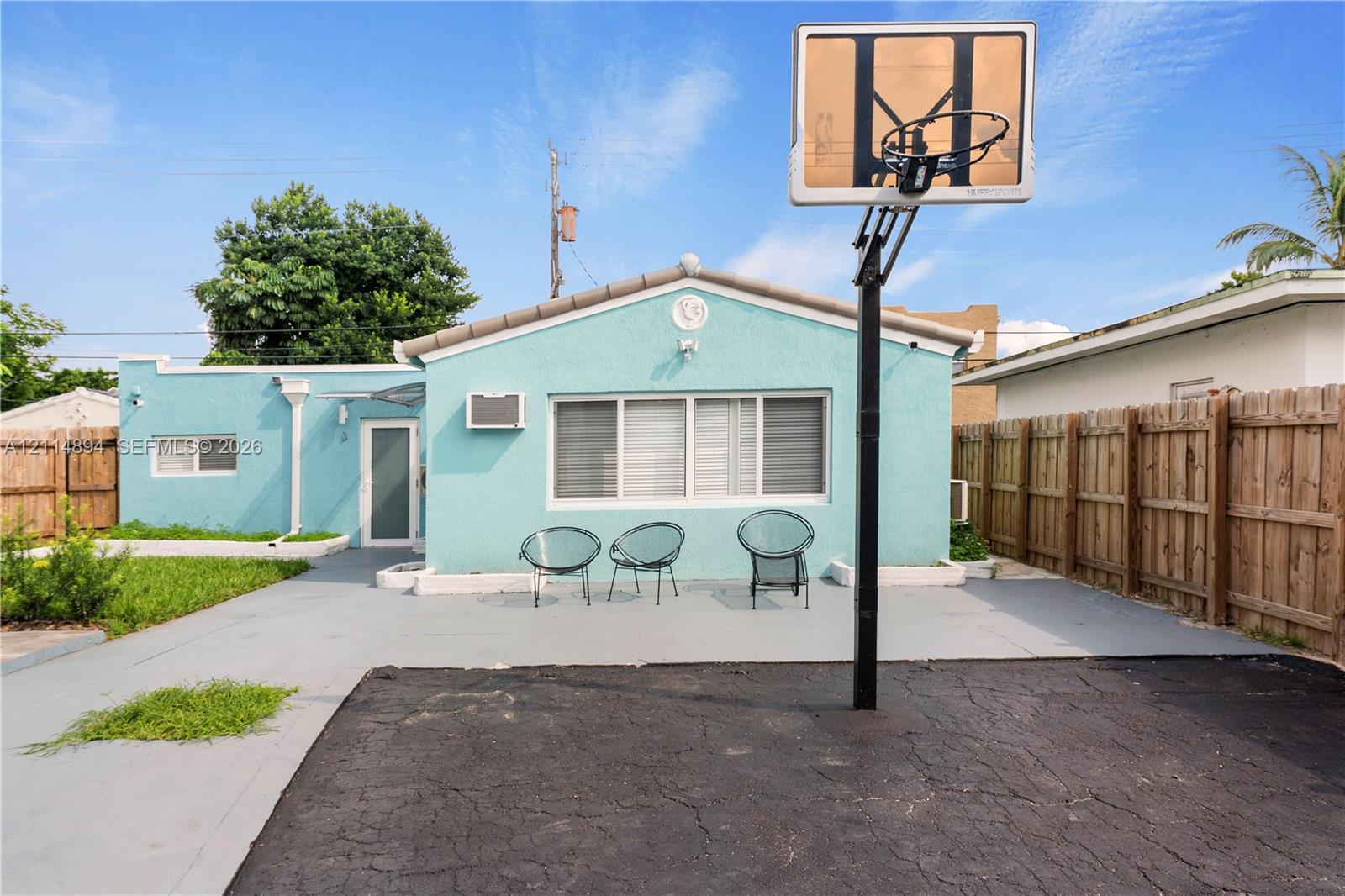 Exterior features include a stucco finish, paved patio surface, basketball hoop, and wood-panel privacy fencing