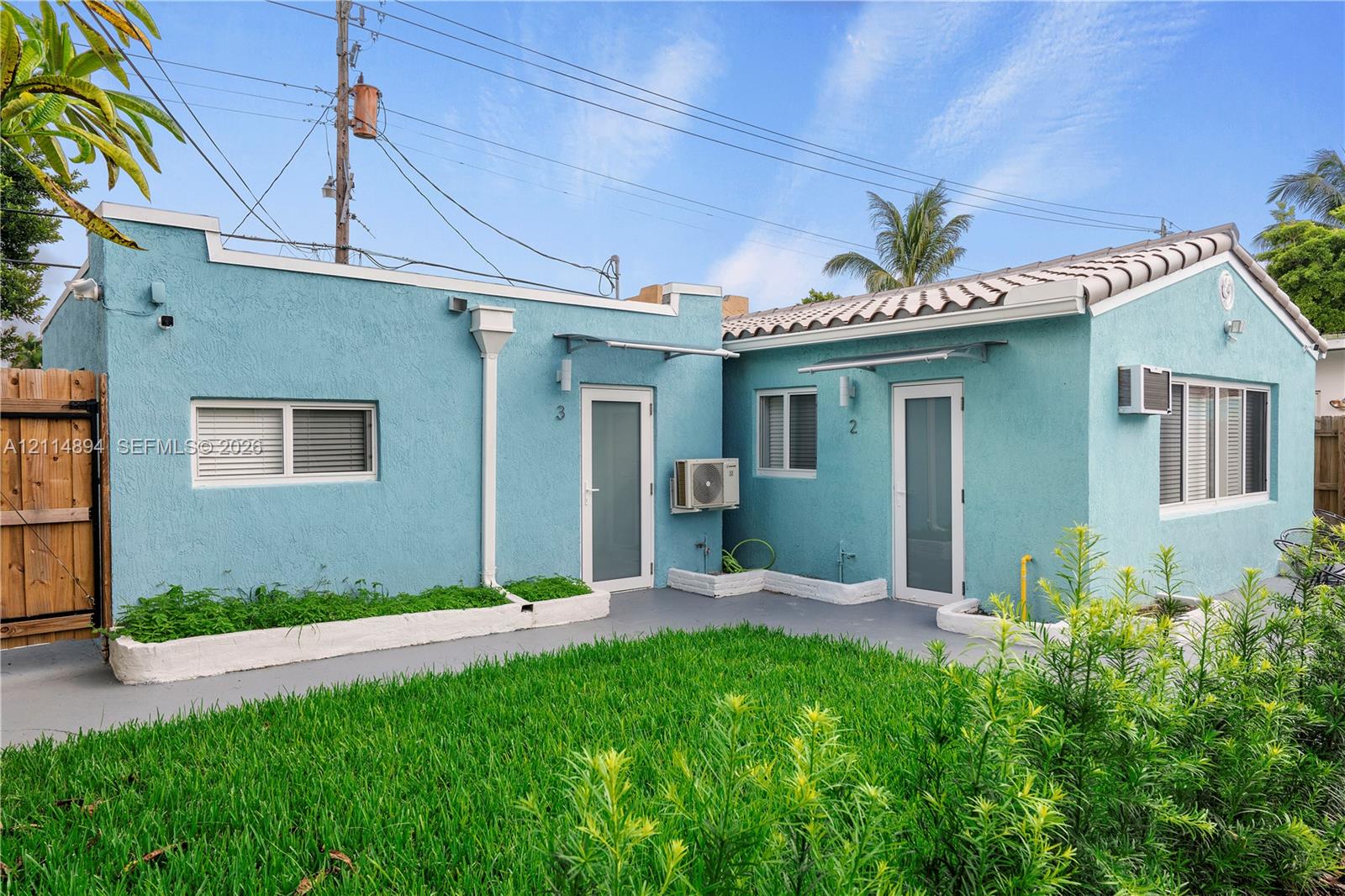 Stucco exterior featuring dual entryways, tile roof accents, and a grass courtyard with perimeter planting beds