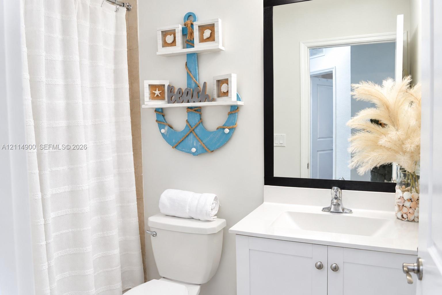 Bathroom vanity featuring a white cabinet base, stone countertop, integrated sink, and a rectangular mirror with a black frame
