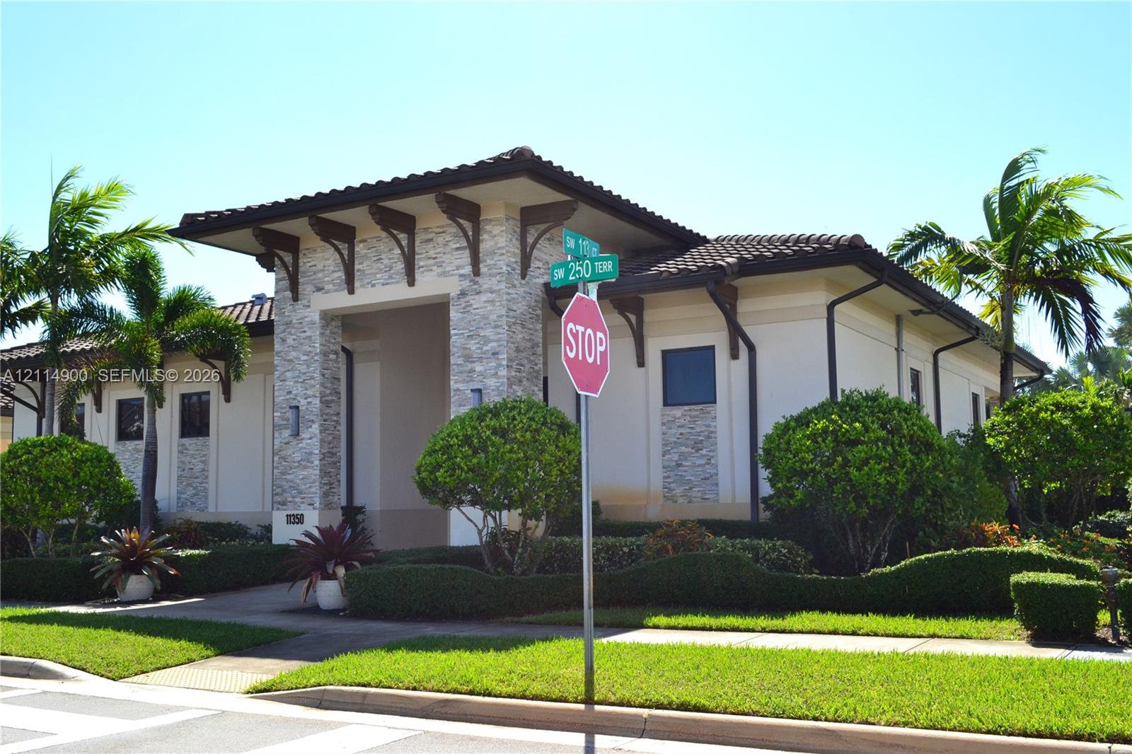 Single-story exterior featuring a stone-clad portico, decorative wooden roof corbels, low-pitched tiled roofing, and manicured landscaping