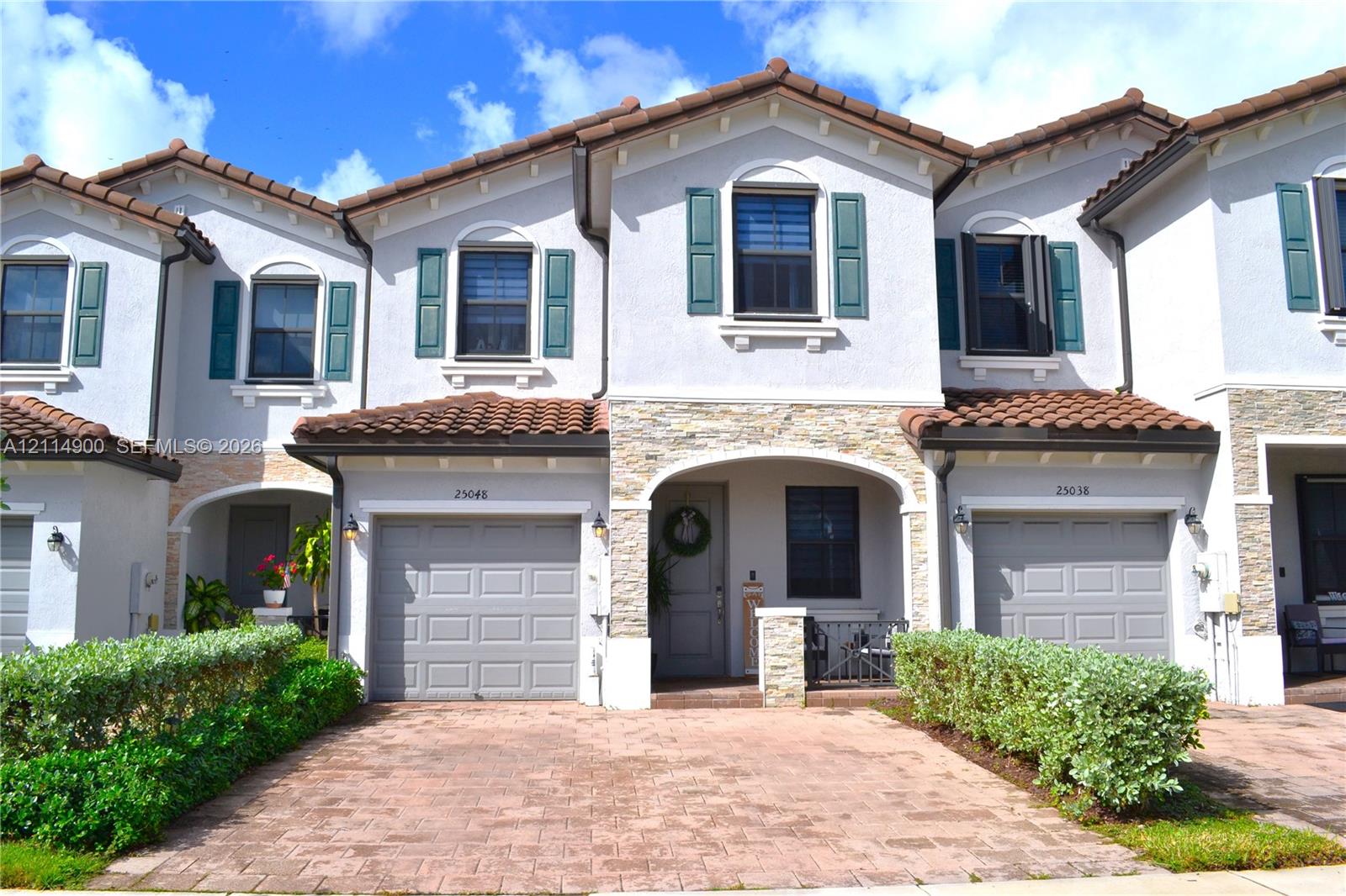 Multi-family exterior featuring a light-toned stucco facade with stone veneer accents, decorative shutters, a clay-tile roof, and a paved brick driveway