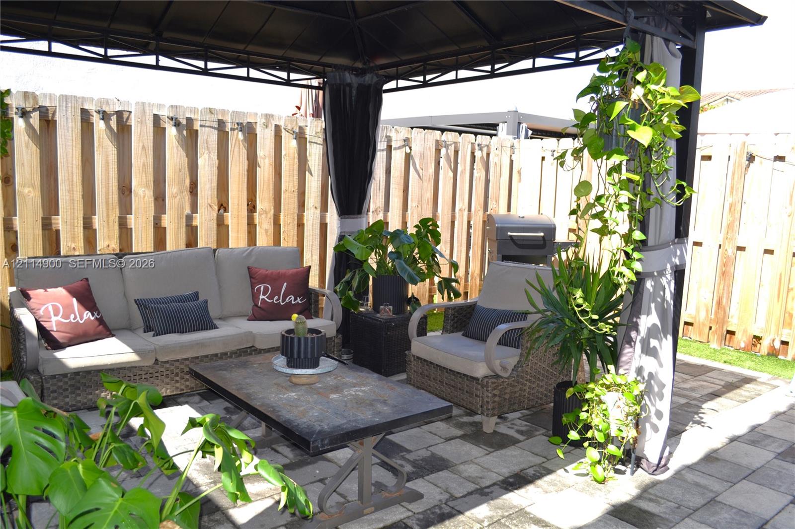 Outdoor gazebo featuring a metal frame, concrete paver patio, and wood-slat privacy fencing