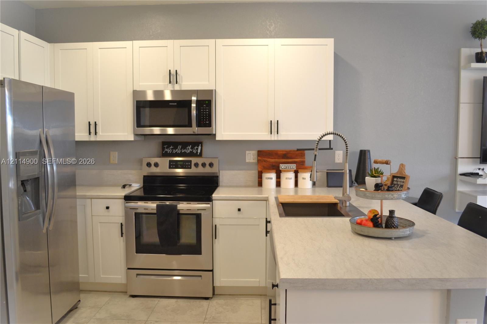 Kitchen featuring white shaker-style cabinetry, stainless steel appliances, neutral countertops, an undermount sink with a pull-down faucet, and a center island