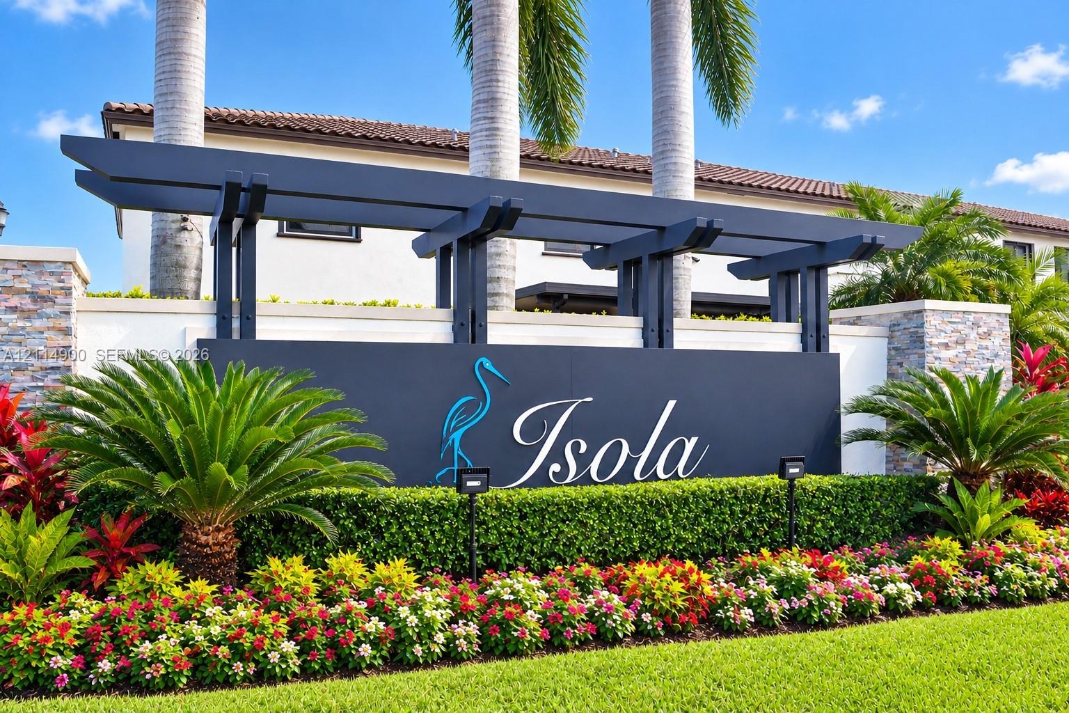 Community entrance featuring a custom architectural monument sign, stone veneer masonry, pergola-style structure, and professional tropical landscaping
