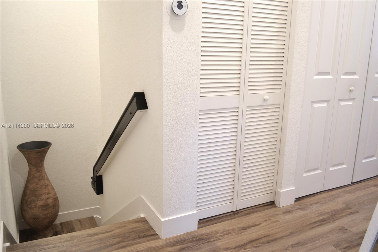 Wood-finish flooring, white louvered bifold closet doors, and a mounted black handrail