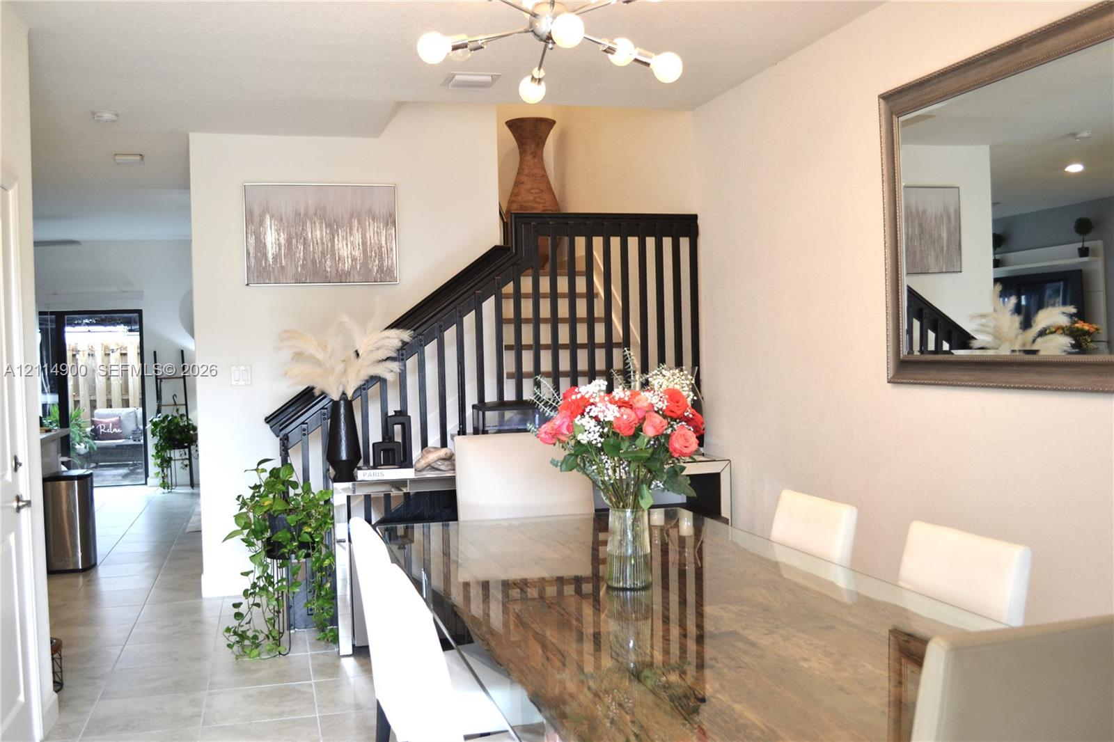 Neutral tile flooring, multi-arm sputnik-style chandelier, and black-painted wooden staircase balusters