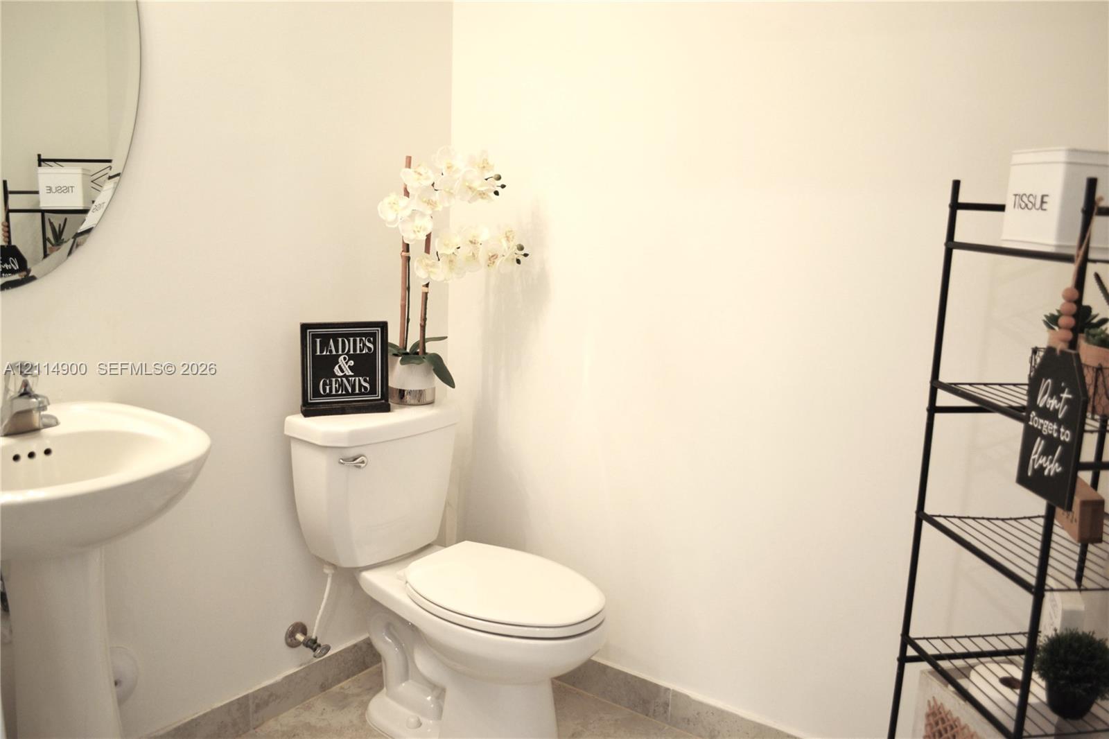 Pedestal sink featuring a polished chrome faucet and an oval wall-mounted mirror, paired with a standard-profile toilet and stone-finish flooring
