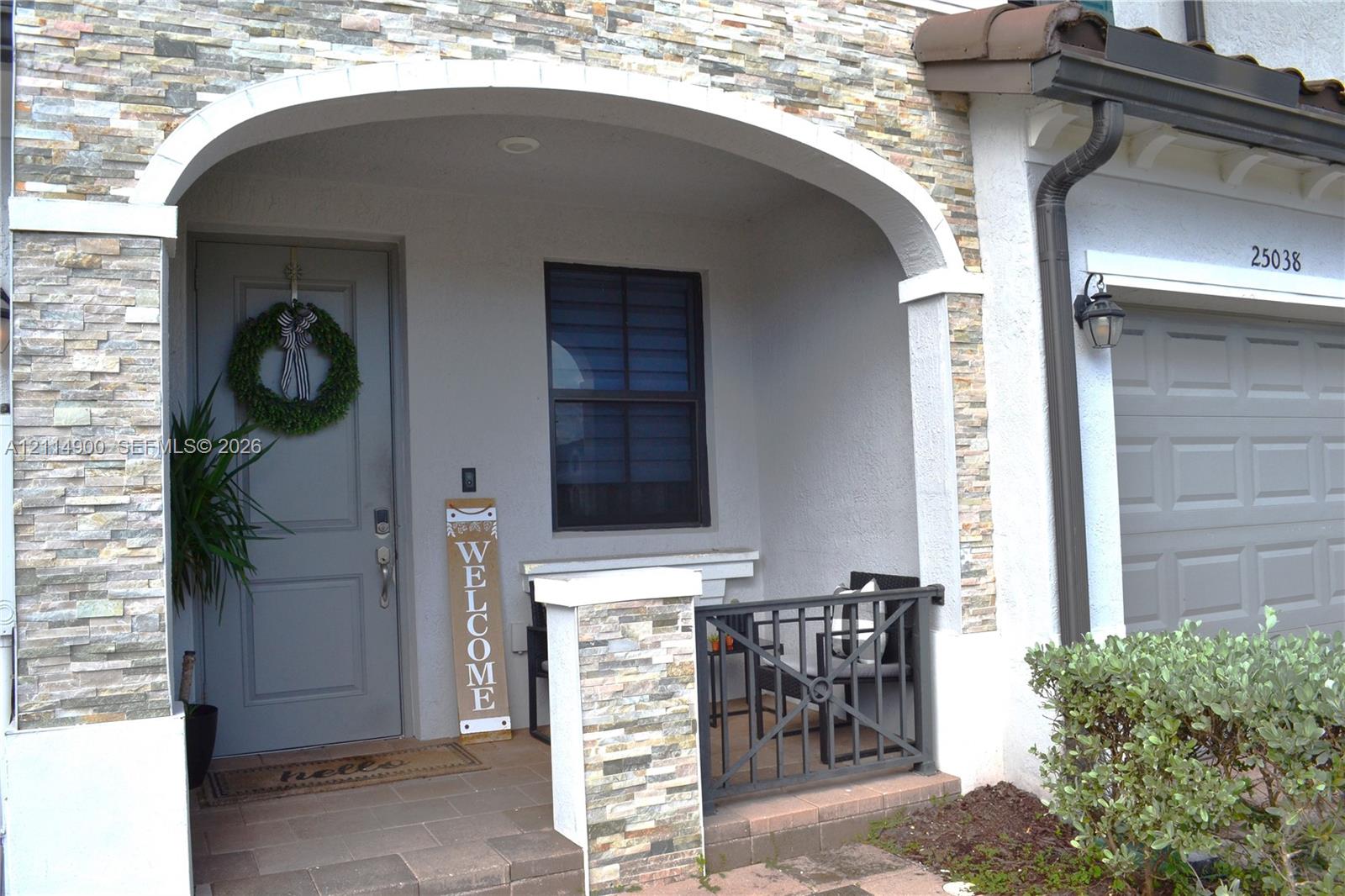 Covered entryway featuring a stone veneer facade, an arched architectural detail, a paver porch, and metal railing
