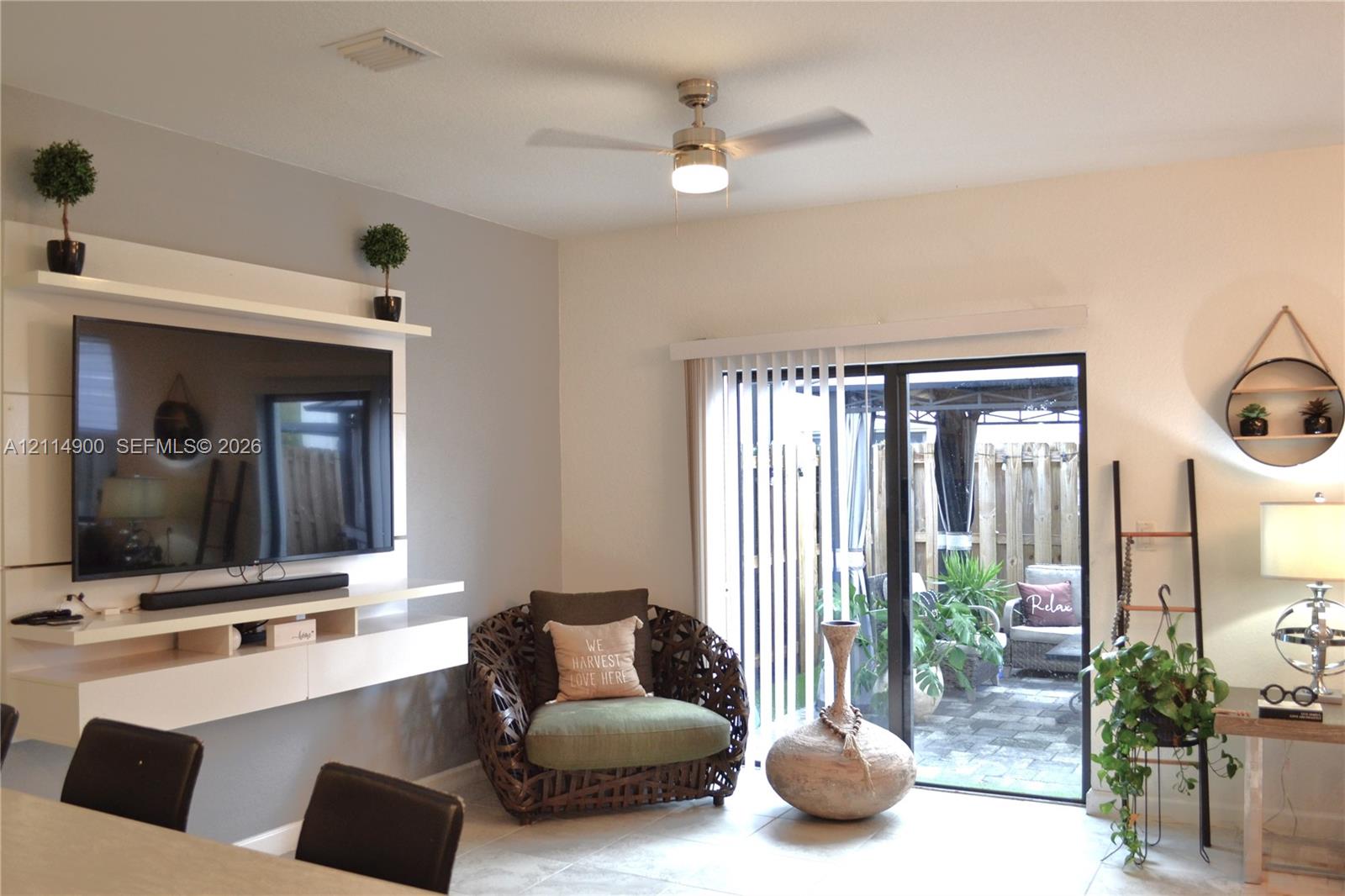 Living area featuring a custom white built-in media console with tiered shelving, sliding glass door with vertical blinds, and a ceiling-mounted light fixture with fan