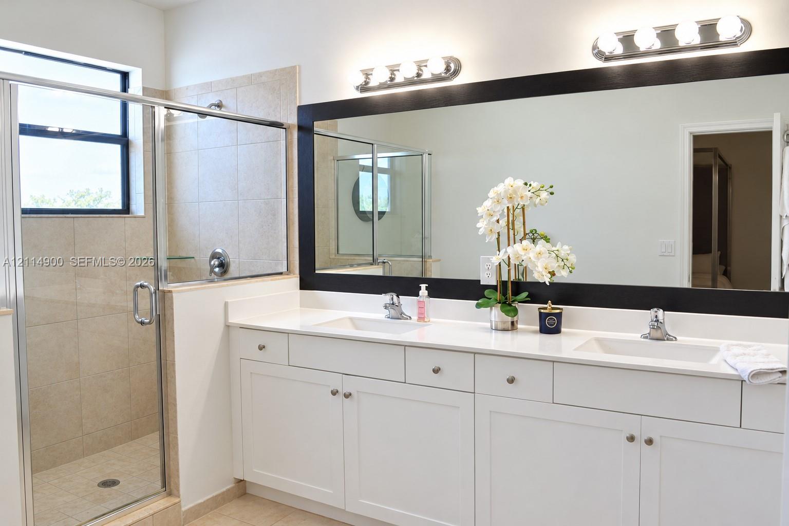 Double vanity featuring white cabinetry, quartz countertop, dual integrated sinks, and polished chrome fixtures, complemented by a walk-in shower with tiled surround and glass enclosure