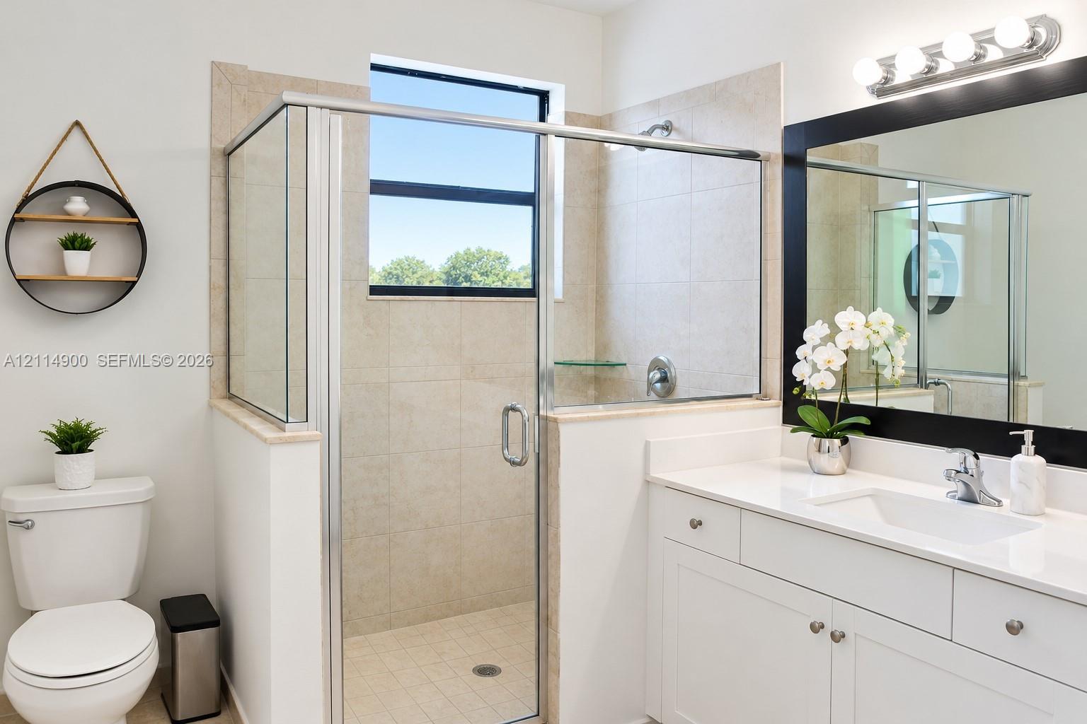Bathroom featuring a glass-enclosed shower with tile surround, white cabinetry, solid-surface countertop, and a framed mirror with integrated lighting